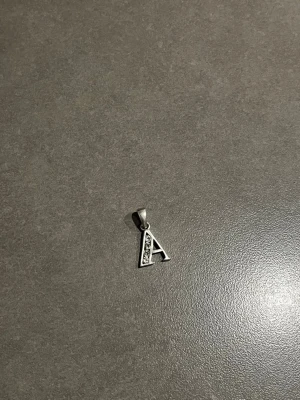 Halsbandshänge bokstav A i silver - Äkta 925 Sterling Silver bokstavsberlock “A” med 4 infattade äkta diamanter på vänster sida av hänget. Elegant och stilren design som passar både vardag och finare tillfällen. Stämplad med 925 på baksidan vilket bekräftar äkta sterling silver.  Berlocken har en exklusiv look med fina detaljer och vackert gnistrande stenar. Perfekt som personlig present eller till någon vars namn börjar på A.  • Äkta 925 sterling silver • 4 äkta diamanter • Tidlös och exklusiv design • Fint skick och passar allt