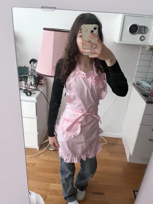 Söt rosa volangförkläde förkläde - Rosa förkläde med volangkant och knytband i midjan och nacken. Förklädet har en feminin och lekfull design med hjärtformad överdel och dekorativa detaljer. Perfekt för dig som gillar kawaii-stil eller vill ha något extra gulligt i köket.
