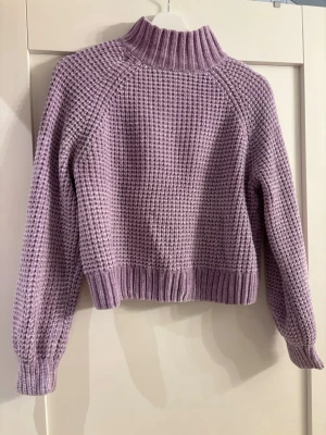 Ljuslila stickad polotröja - Mysig ljuslila stickad tröja med hög polokrage och grov struktur. Tröjan har långa ärmar och ribbade muddar vid ärmslut och nederkant. Perfekt för kalla dagar och enkel att styla till jeans eller kjol. Supermjukt material!