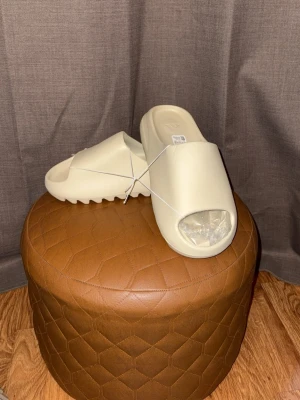 Beige slidesandaler i chunky modell - Säljer ett par trendiga beige slidesandaler med öppen tå och bred rem. Sandalerna har en chunky sula med räfflad undersida för extra grepp. Tillverkade i ett mjukt och flexibelt syntetmaterial, perfekta för en avslappnad och modern stil.