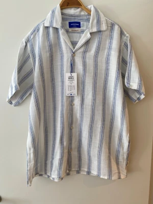 Randig skjorta från Jack & Jones - Säljer en vit skjorta från Jack & Jones med blåa vertikala ränder. Aldrig använt (fel storlek och glömde returnera). Storlek L. Nypris 499kr. 