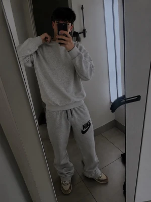mjukisbyxor Nike - Gråa mjukisbyxor från Nike med svart logga på vänster lår. Byxorna har resår i midjan med två fickor framtill. Tillverkade i mjukt och bekvämt material, perfekta för en avslappnad look, eller till träning.