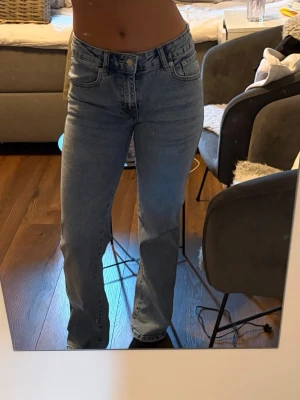 Ljusblå bootcut jeans från Lager 157 - Säljer ett par ljusblå jeans från Lager 157 med bootcut passform och klassiska fem fickor. Jeansen har medelhög midja och är tillverkade i denim med en snygg tvätt. Bakfickorna har lock och knappdetalj. 