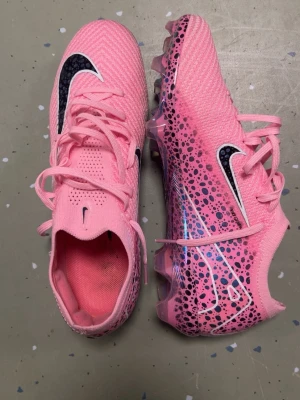 Nike rosa fotbollsskor med mönster - Säljer ett par grymma rosa fotbollsskor från Nike med svart och vitt swoosh-märke. Skorna har ett coolt prickigt mönster i svart och lila på sidorna och genomskinliga, storlek 41 men passar bättre som 42 or 