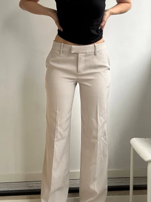 Beige kostymbyxor med raka ben - Snygga kostymbyxorna en kall beige färg. Byxorna har aldrig använts därav prislappen på. De är lowwaist vilket jag inte gillar på mig själv. 