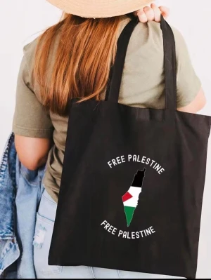 Svart shoppingväska Free Palestine - Svart shoppingväska i tyg med tryck av texten 'Free Palestine' och en karta med Palestinas flagga. Väskan har långa handtag och rymlig form, perfekt för att bära med sig allt man behöver. Snygg och enkel design som sticker ut.