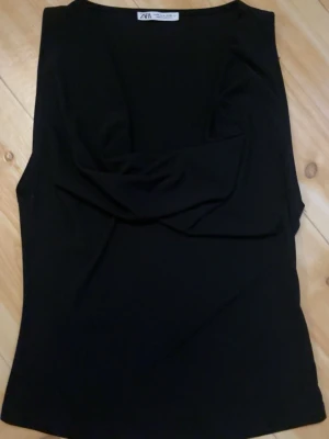Svart ärmlös topp från Zara - Snygg svart ärmlös topp från Zara som är tajt men har draperad detalj framtill. Denna toppen säljs inte mer. Tunn och mjuk i materialet, enkel att matcha och passar till många olika outfits till fester och vardagen. (Har en bild med den på dock inte så tydlig men kom privat för fler bilder)