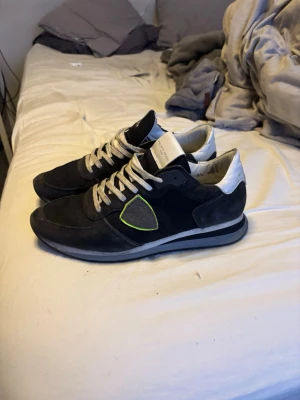 Philippe Model svarta sneakers - Svarta sneakers från Philippe Model med detaljer i mocka och läder. Skorna har vita snören, vit hälkappa och en grå sula. På sidan finns en grå sköld med gul kant. Snygg och sportig design som passar till många outfits.