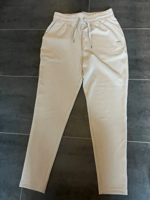 Beige mjukisbyxor från Aimn - Snygga beige mjukisbyxor med elastisk midja och dragsko. Byxorna har raka ben och sidofickor, perfekta för en avslappnad stil. Tillverkade i mjukt material. Nypris är 799. Kom gärna med prisförslag.