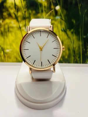 Vit och guldig minimalistisk klocka - Stilren klocka med vit urtavla och guldiga detaljer. Armbandet är vitt och har en klassisk design som passar till många olika stilar. Urtavlan är enkel utan siffror, vilket ger ett modernt och cleant intryck. Perfekt accessoar för dig som gillar enkelhet och elegans.