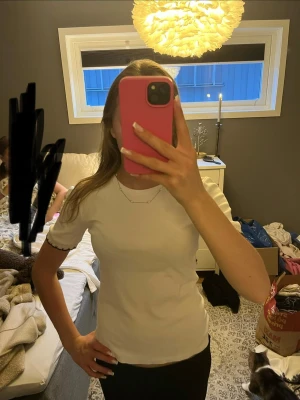 Vit t-shirt med mönster runt kanterna - Vit t-shirt med svarta och guldiga mönster vid ärmarna, knappt använd💕.
