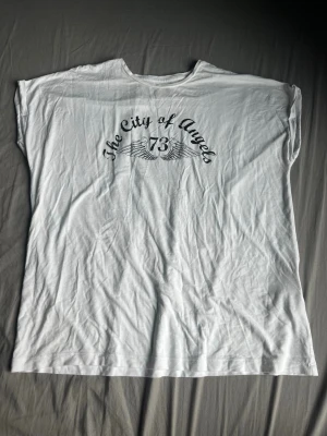 Vit t-shirt med tryck City of Angels - Vit t-shirt med svart tryck där det står 'The City of Angels 73' och har vingar som motiv. Klassisk rund hals och korta ärmar. Perfekt för en avslappnad och cool stil.