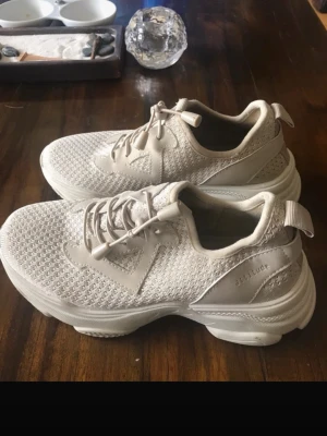 Beige sneakers från Altitude - Snygga beige sneakers från Altitude med stickad mesh-överdel och detaljer i syntet. Skorna har elastiska snören med dragsko och en chunky sula för extra komfort. Perfekta för en avslappnad och trendig stil.