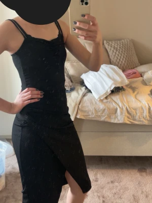 Svart ribbad klänning Even&Odd - Säljer en svart ribbad klänning från Even&Odd med smala axelband och slits framtill. Klänningen har en figurnära passform och är tillverkad i ett stretchigt material som sitter snyggt på kroppen. Perfekt för dig som gillar en enkel men stilren look.