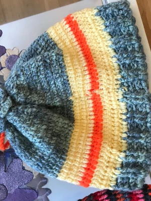 Retro virkad mössa i pastellfärger - Unik handvirkad mössa i retrostil med breda ränder i ljusblått, gulvitt och orange. Mössan har en mjuk och stretchig passform och är tillverkad i tjockt garn, perfekt för dig som vill sticka ut med färg och vintagekänsla. Materialet känns som akryl eller ullblandning.