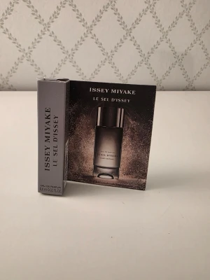 Issey Miyake Le Sel d'Issey parfym - Issey Miyake Le Sel d'Issey Eau de Parfum i miniflaska på 0,6 ml. Flaskan är cylinderformad i genomskinligt glas med svart lock. Förpackningen är elegant i grå och silvertoner med stilren text. Perfekt för dig som vill testa en exklusiv doft.