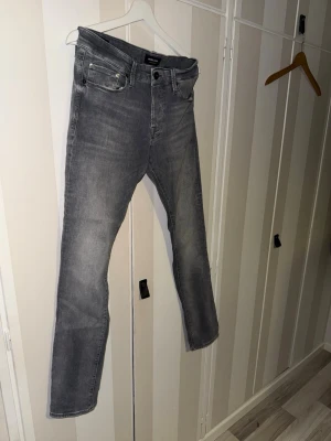 Grå slim fit jeans från Jack & Jones - Snygga grå slim fit jeans från Jack & Jones med klassisk femficksdesign och diskreta slitningar. Jeansen har normal midja, raka ben och är tillverkade i ett mjukt denimtyg med lite stretch för extra komfort.      W31-L32