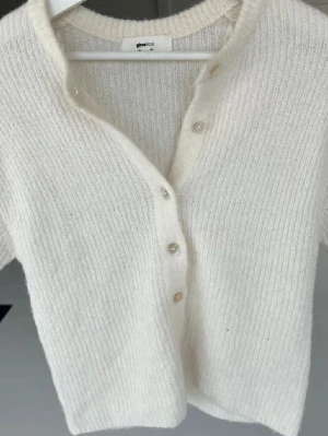 Vit kortärmad kofta  - Söt vit kofta med korta ärmar och rund halsringning. Koftan har en rak passform och knäpps med vita knappar framtill. Tillverkad i ett mjukt, ribbat material som ger en mysig känsla