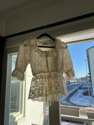 Vit spetsblus med trekvartsärm - Vit spetsblus med fina detaljer och knytband i midjan. Blusen har rundad halsringning, volangkant och trekvartsärmar.