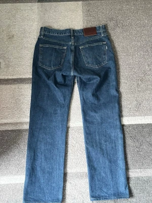 Raka Edwin Jeans - Säljer ett par blå Edwin jeans i klassisk rak modell med fem fickor och normal midja. Jeansen har en mörkblå tvätt och är tillverkade i denim. Perfekta för en avslappnad och tidlös stil.