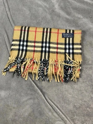 Beige halsduk från Burberry - Klassisk beige halsduk från Burberry med ikoniskt rutigt mönster i svart, vitt och rött. Ny!