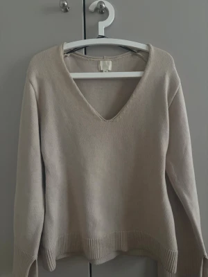 Beige stickad tröja från H&M - Snygg beige stickad tröja från H&M med djup V-ringning och slit vid armarnas slut, använd några gånger o lite små fläckar som man ser i bild två men inget som märks✨