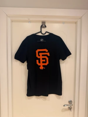 Svart SF Giants t-shirt - Säljer en svart t-shirt från 47 Brand med stort orange San Francisco Giants-logotyp på bröstet. Klassisk passform med rund hals och korta ärmar. Perfekt för dig som gillar sportiga och stilrena plagg.                                   Modellen är 185cm lång och väger 82kg.          Använd 1 gång.