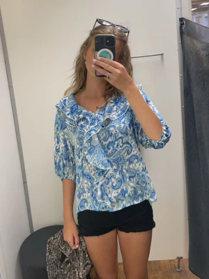 Blå paisleymönstrad blus med volang - Supersöt blus i blått och vitt paisleymönster. Blusen har volangdetaljer och trekvartsärm. Den är använd fåtal gånger och har inga defekter.