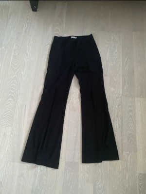 Svarta utsvängda kostymbyxor - Snygga svarta kostymbyxor med utsvängda ben och hög midja. Klassisk design utan synliga fickor eller detaljer, perfekta för en stilren look. Materialet ser ut att vara en mjuk och följsam textil som ger en skön passform.