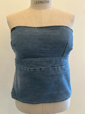 Blå denim tubtopp - Trendig blå tubtopp i denim med enkel, rak passform. Toppen är axelbandslös och har en söm tvärs över mitten för en cool detalj. Perfekt att styla med höga jeans eller kjol för en avslappnad vibe. Delvis omsydd.