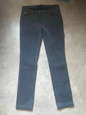 Mörkgrå slim fit jeans - Snygga mörkgrå slim fit jeans med klassisk femficksdesign och smala ben. Jeansen har knapp- och dragkedjestängning samt silverfärgade nitar. Perfekta för en clean och stilren look.