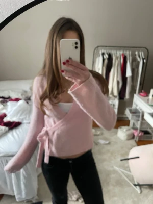 Ljusrosa omlottkofta - Söt ljusrosa omlottkofta med knytband i midjan och långa ärmar. Koftan har en mjuk, fluffig känsla och en avslappnad passform som ger en trendig look. Perfekt att styla över ett linne eller topp.