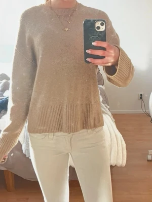 Beige stickad tröja med ribbad kant - Mysig beige stickad tröja med rund hals och bred ribbad kant nedtill samt vid ärmsluten. Tröjan har en avslappnad passform och långa ärmar. Perfekt för lager på lager och enkel att matcha med olika stilar.