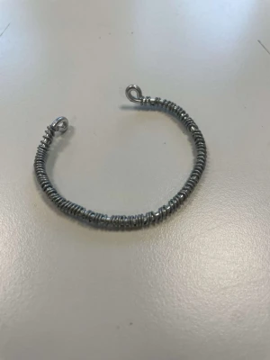 Justerbart armband i silverfärg - Armbandet är gjort av silverfärgad metalltråd med en tunnare metalltråd som är virad runt. Storleken på armbandet går att justera så att det passar din arm perfekt. 