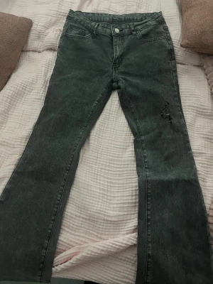 Grå bootcut jeans från SHEIN - Säljer ett par grå bootcut jeans från SHEIN i storlek S (EU 36). Jeansen har en lätt tvättad look, klassiska fem fickor och en liten sliten detalj på ena benet. Materialet är bomull med lite elastan och viskos för extra komfort. Dem är sönder där man har bältet men de går o fixa!