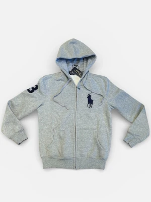 Grå hoodie från Polo Ralph Lauren - Snygg grå hoodie med dragkedja från Polo Ralph Lauren. Stor mörkblå logga på bröstet och siffran 3 på ärmen. Utrustad med huva och dragsnören samt två fickor framtill. Tillverkad i mjuk bomullsblandning för skön komfort.