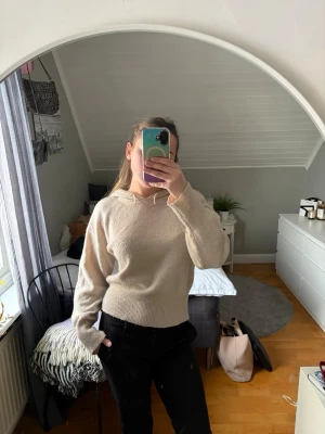 Beige stickad tröja med luva - En enkel och stilren beige stickad tröja med luva och långa ärmar. Tröjan har ribbstickade muddar vid ärmslut och nederkant, vilket ger en snygg passform. Perfekt för att skapa en avslappnad look.