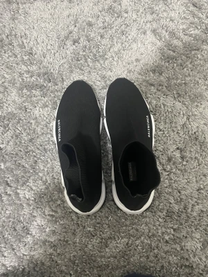Balenciaga Speed Trainer sneakers svart - Säljer ett par svarta Balenciaga Speed Trainer sneakers med vit sula och stickad ovandel. Skorna har en strumpliknande passform och Balenciaga-logga på sidan. Sulan är chunky och ger en futuristisk vibe. Perfekta för dig som gillar streetwear och vill sticka ut.
