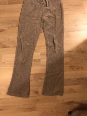 Grå mjukisbyxor med dragsko - Mysiga grå mjukisbyxor med flear ben och dragsko i midjan. Byxorna har fickor på sidorna och är tillverkade i ett mjukt, fleeceliknande material som känns skönt mot huden. Perfekta för chill dagar hemma eller när du vill vara extra bekväm.