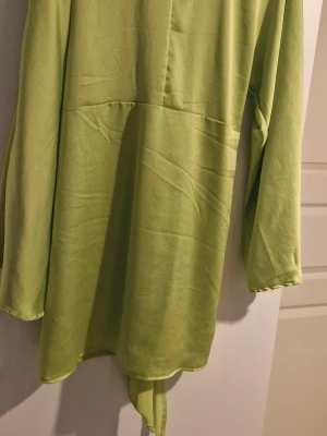 Ljusgrön långärmad klänning  - Trendig ljusgrön klänning långa ärmar och avslappnad passform. Tillverkad i ett mjukt, lätt tyg som ger en skön känsla. Klänningen en enkel design med rund hals och knytband nedtill för extra detalj.