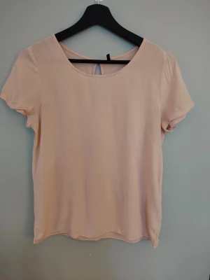 Ljusrosa blus med kort ärm från ONLY  - Söt ljusrosa blus med rund halsringning och korta ärmar. Tillverkad i ett mjukt, tunt material som ger en luftig känsla. En liten öppning bak i nacken ger en extra detalj. Perfekt att matcha med jeans eller kjol. Är i fint använt skick, har en liten obehandlad fläck på framsidan. Storlek S. 