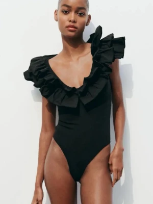 Svart baddräkt med volangdetaljer - Stilren svart baddräkt med djup v-ringning och stora volanger runt axlar och urringning. Baddräkten har en figurnära passform och högt skurna ben. Perfekt för dig som vill sticka ut på stranden med en trendig look.