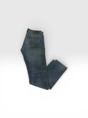 Blå raka jeans från Lee - Säljer ett par klassiska blå jeans från Lee med rak passform och femficksmodell. Jeansen har en snygg tvättad look och Lee-logga på bakfickan samt läderpatch i midjan. Perfekta till vardags för en avslappnad stil.