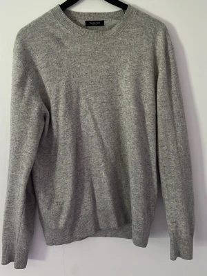 Grå stickad tröja Massimo Dutti - Klassisk grå stickad tröja från Massimo Dutti i mjuk kashmirblandning. Tröjan har rund halsringning, långa ärmar och ribbade muddar vid ärmslut och nederkant. Perfekt basplagg för lager på lager och enkel att matcha. Storlek L men passar mer som M