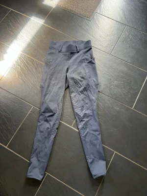 Mörkblå ridleggings med fickor - Snygga mörkblå ridleggings med hög midja och praktiska sidofickor. Silikonmönster på insidan av benen för extra grepp i sadeln. Stretchigt material som ger bra rörelsefrihet. Två bakfickor med knappdetaljer för en sportig look. Passar Xs,S
