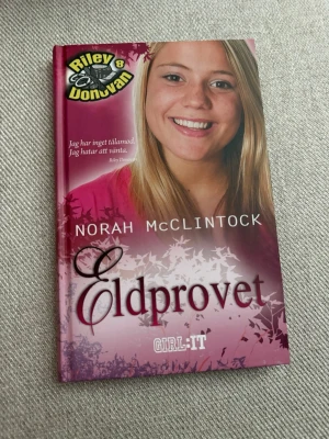 Eldprovet av Norah McClintock - Eldprovet är en ungdomsroman av Norah McClintock i Riley Donovan-serien. Boken har ett hårt omslag i rosa och lila toner med vita och svarta detaljer. Perfekt för dig som gillar spänning och mysterier i skolmiljö.