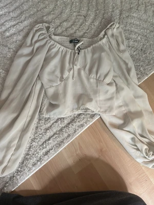 Beige blus från Gina Tricot - Säljer en beige blus från Gina Tricot med puffiga ärmar och snörning framtill. Blusen har en snygg, figurnära passform och är gjord i ett lätt, flowigt material som känns skönt mot huden. Perfekt för dig som gillar trendiga och romantiska plagg.