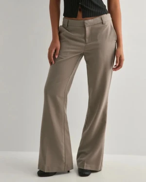 Beige vida kostymbyxor - Snygga beige kostymbyxor med vida ben och låg midja. Byxorna har bälteshällor, diskreta sidofickor och stängs med dragkedja och hake. Perfekta för en clean och stilren look. Materialet ser ut att vara en mjuk och lätt blandning, vilket ger en skön känsla.
