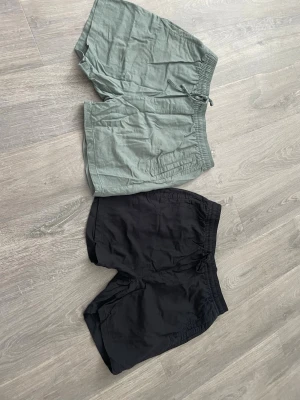 Två par shorts i svart och grön - Två par shorts, ett par i svart och ett par i ljusgrön. Båda har elastisk midja och snörning framtill för justerbar passform. Perfekta för varma dagar och avslappnade tillfällen. Tillverkade i ett lätt och luftigt material.