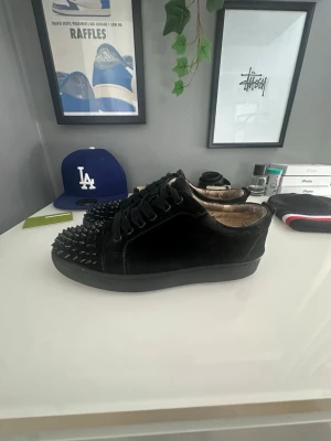 Svarta sneakers med nitar Christian Louboutin - Unika svarta sneakers från Christian Louboutin med mattsvarta nitar på tån och ovansidan. Skorna är låga och har en klassisk siluett med snörning. Tillverkade i mocka för en lyxig känsla och cool edge. Perfekta för dig som vill sticka ut. Kan sänka till 700kr vid snabb affär 